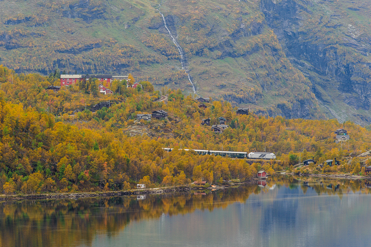 Flåmsbanen, the Flåm line, is one of the steepest railways in the world not using cogs, with a 5,5% gradient. A train towards Flåm is seen across Reinungavatnet, with Vatnahalsen hotel in the background. 